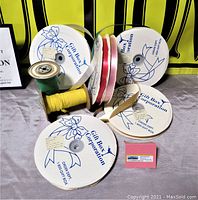 Photo showing various full and partial ribbon rolls on round white spools with Gift Box Corporation logo and ribbon colors red, white, pink, yellow, and green.
