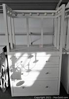 White baby changing station shown from front side. Three drawers with metal knobs visible. Frame structure on top for changing surface visible.