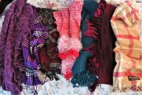 Lot of 7 scarves in various colors and textures including plaid, knit, and cashmere shown spread out on bed.