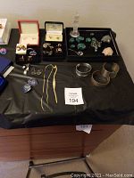 Overall view of trays displaying stone carvings on right and boxes of earrings and cufflinks on left, plus bracelets and chains front center