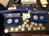 Two blue display cases with US Liberty $1 and half dollar coins, loose state quarters in protective plastic cases spread around them.