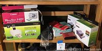Photo shows Canon PowerShot S400 digital camera box, VuPoint Photo Cube printer box, two Kodak ink cartridge packs, and various camera cases and straps on a wooden shelf.