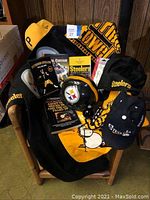 Photo of Pittsburgh Steelers mini helmet, black and yellow scarf, multiple ball caps, and Steelers books arranged on a wooden chair.