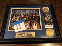 Framed Golden State Warriors 2017 NBA Champions plaque showing team photo, playoff ticket stub replica, and two golden medallions.