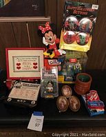 Full view of lot contents including Minnie Mouse figure, Halloween buttons, Simpsons toys, sports communicator, framed cross-stitch, photos, and small collectibles.