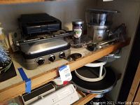Shelf with Cuisinart 5-in-1 Griddler, Salton Belgian Waffle Maker, and Breville Juicer with accessories