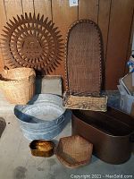 Photo showing entire lot of baskets, tubs, trays, metal container, wooden box, and decorative rusty metal sun on floor against wood-paneled wall.