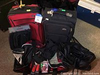 Photo showing two medium rolling suitcases (red Samsonite, black Victorinox), Victorinox packing cubes, combination suitcase locks, black duffel bag, and black fanny pack arranged on carpeted floor.