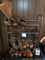 Metal shoe rack holding various boots and shoe care products on wooden panel background.