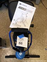 Rodeo Core exercise machine with instruction manual, resistance band, and exercise ball placed on black stool.