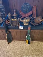 Overview of collection showing rice scoops, ashtrays, tea pitcher, beggar bowl, oil lamp, and wooden comb on a wooden shelf against wood panel wall.