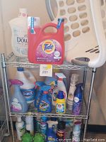 Photo of assorted laundry supplies including detergent, softener, spot cleaners, white laundry basket, and white metal rolling cart in laundry room.