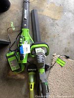 Sun Joe electric leaf blower and string trimmer with battery charger and rechargeable battery laid on concrete floor, showing green and black color scheme.
