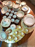 Full view of multiple china sets arranged on wooden table including plates, bowls, teacups, and placemats
