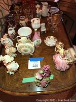 Overview of assorted glassware, ceramic, and figurines placed on wooden table surface showing variety of collectibles in the lot.