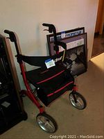 Side angle view of the red frame drive rolling walker showing two large silver front wheels, black seat, and handbrakes on handles.