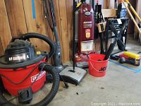 Craftsman red and black 8-gallon wet/dry vacuum with hose, Bissell and Dirt Devil sweepers, and red Eureka upright vacuum with bucket containing parts.