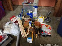 Full view of assorted paint supplies, including brushes, rollers, paint cans, and accessories arranged on a floor.
