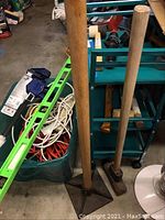 Tools including sledge hammers and ax standing by green metal tool cart with plastic bin of extension cables and green level resting across bin.