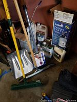 Photo of deck care supplies including cleaning liquids, stain applicator stick, deck care sprayer, broom, shovel, and window wiper.