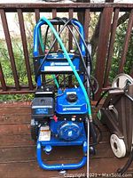 Front view showing blue frame, black engine, hoses and spray wand on wooden deck