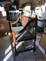 Side view of wooden Deacon bench showing the armrest, turned legs, and floral upholstered cushions.