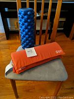 Photo showing blue textured foam roller and orange Spoonk Space acupressure mat resting on a chair.