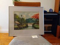 Frontal photo of the Indonesian watercolor painting in silver frame placed on chair, showing artwork and matting clearly.