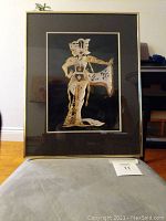 Framed Indonesian woman print showing traditional attire in gold and beige tones on black background.