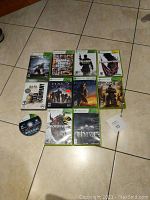 Photo shows eleven Xbox and Xbox 360 video games arranged on tiled floor. Game titles include Thief, Prototype 2, Gears of War 3, Prototype, Call of Duty 3, Halo Reach, Halo 4, Grand Theft Auto 5, Halo 3, Battlefield Bad Company, and a single disc of Watch Dogs.