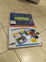 Photo of both the Knowledge board game and the Electronic Snap Circuits kit boxes on tile floor.