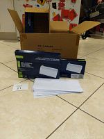 Nine boxes of envelopes with some envelopes removed and placed in front, boxes are navy blue with white text and green highlights, envelopes white and rectangular sized about 4x9 inches