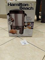 Box of Hamilton Beach Brew Station Coffee Urn labeled with 40 cup capacity, showing easy fill and clean feature and image of the urn dispensing coffee into a mug.