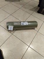 Rolled Therm-a-Rest sleeping pad in green color wrapped in plastic packaging with brand label visible on tiled floor.