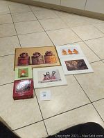 Lot showing two puzzle boxes and four prints laid out on tiled floor. Puzzles are 100 pieces, prints vary between 10x8 and 11x15 inches sizes.