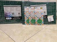 Photo of two green 12x18 inch cutting mats with grid patterns and three packages of Tandy Leather Pearl Headpins in their original packaging