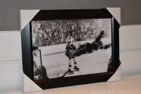 Front view of the framed black and white print showing the hockey player airborne near the goal with crowd in the background, corners protected with wrap.