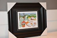 Framed artwork "Skaters in Winter" by Maud Lewis showing the full framed piece with protective corner covers.