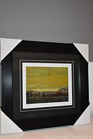Photo showing the framed and matted artwork with protective corner covers still on the black frame, displaying "Wild Geese" print featuring wild geese flying over landscape.
