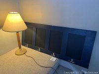 Lamp standing beside wall hanging coat rack featuring four chalkboard panels with dual coat hooks below each panel.