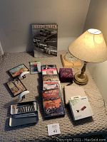 Photo of entire lot showing hardcover book, DVDs, internet stick, vintage clock, small box and lamp on beige carpet against gray wall.