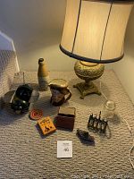 Overall lot displayed on carpet, shows lamp, Toby Mug Jug, pottery bottle, insulator, playing cards, metal cat planter, spinning top toy, and other small items.