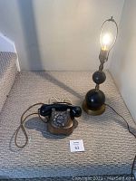 Photo showing vintage rotary dial telephone and Art Deco style lamp placed on carpeted floor near stairs.