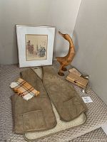 Lot showing all items: framed city print, sheepskin vest, wooden duck, wooden box, clutch, glass bottles, and napkin arranged on carpeted floor.