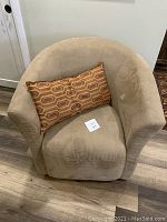 Front and side view of beige faux-suede swivel armchair with a geometric patterned rectangular cushion on the seat, showing slight wear and overall good condition.