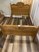 Full view of antique wooden bed frame showing headboard, footboard, and side rails on wood flooring.