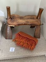 Front view of the antique wooden camel saddle with leather seat and the orange fringe blanket folded in front.