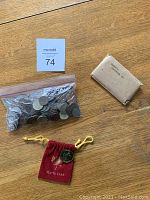 Full view of the lot on wooden floor showing a plastic bag of coins, a red velvet pouch with a gold-colored Maple Leaf coin, and a brown paper envelope souvenir pack.