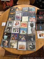 Photo of 23 music CDs arranged on a wooden table including artists like The Eagles, Tom Jones, Rat Pack, Etta James, Johnny Cash, as well as box sets featuring Nat King Cole and Frank Sinatra.