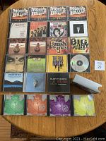 Photo showing 12 music CDs laid flat on a wooden surface, includes multiple multi-disc sets from rock and soundtrack genres.